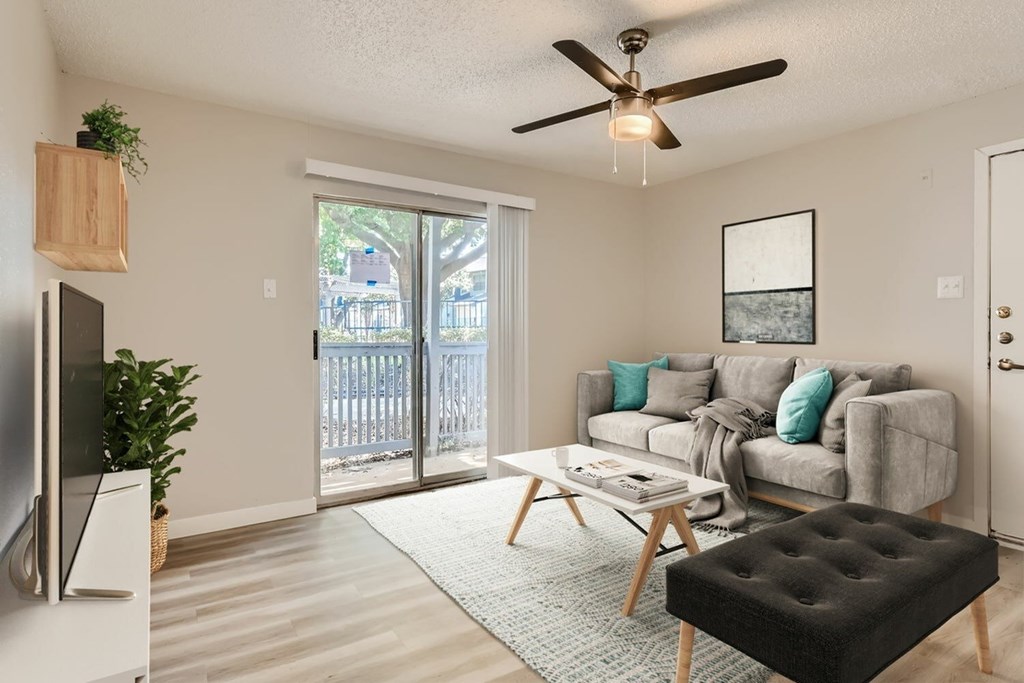 A living room with a grey couch, a black ottoman, and a ceiling fan.