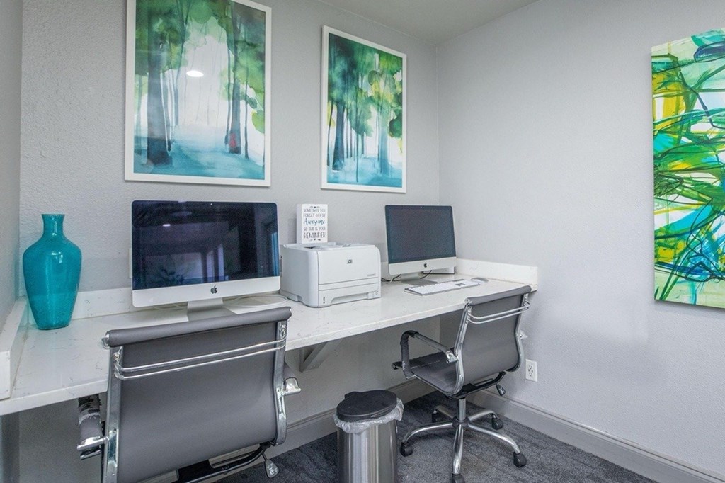 A room with a desk, chairs, and two pictures on the wall.