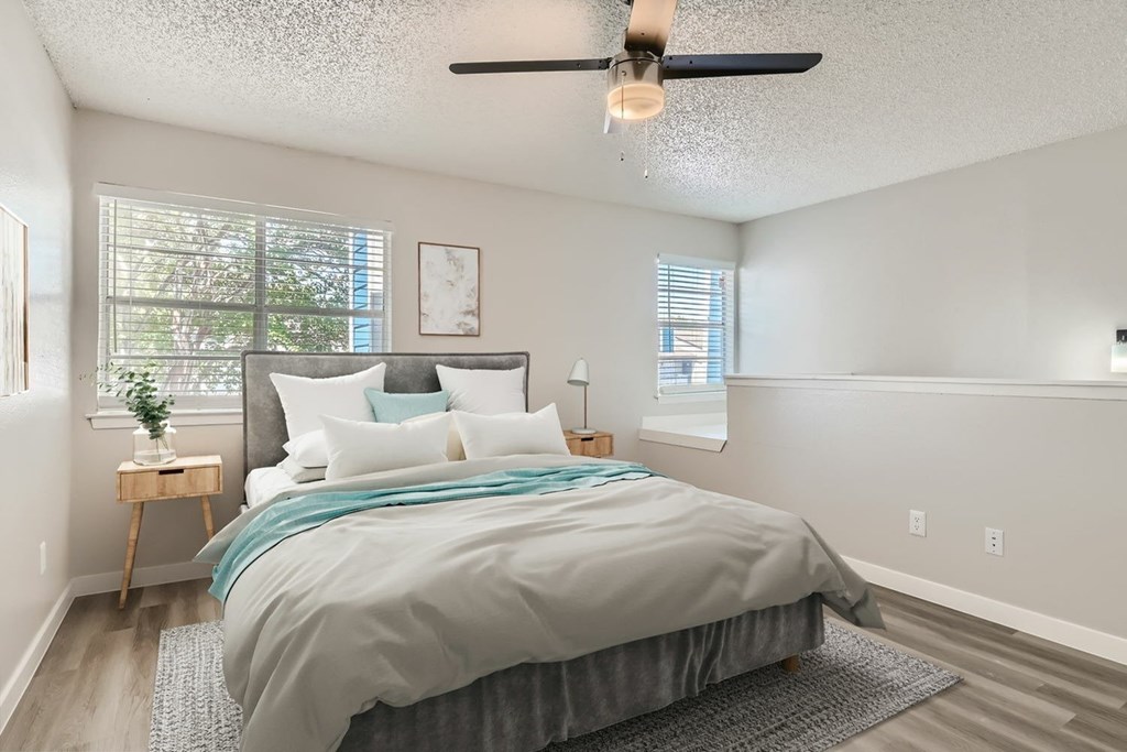 A bedroom with a bed, a ceiling fan, and a window with blinds.