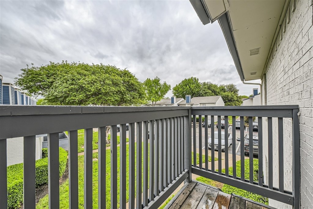 A balcony with a black railing overlooking a green lawn and trees.