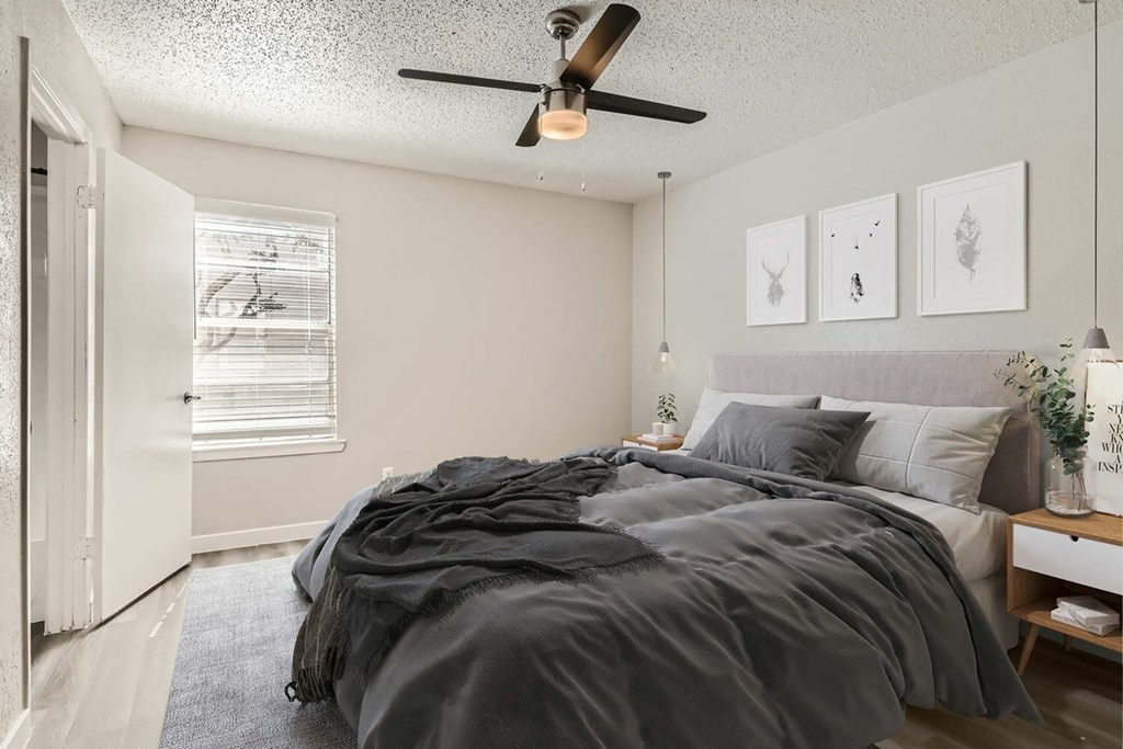 A bedroom with a bed, a ceiling fan, and three framed pictures on the wall.