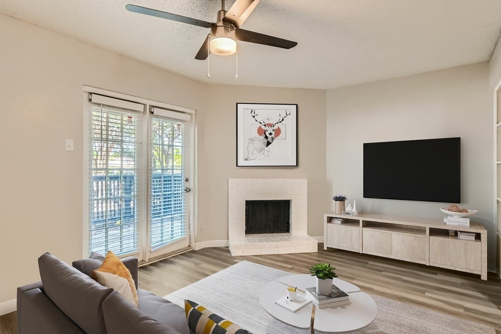 A living room with a grey couch, a fireplace, a television, and a ceiling fan.