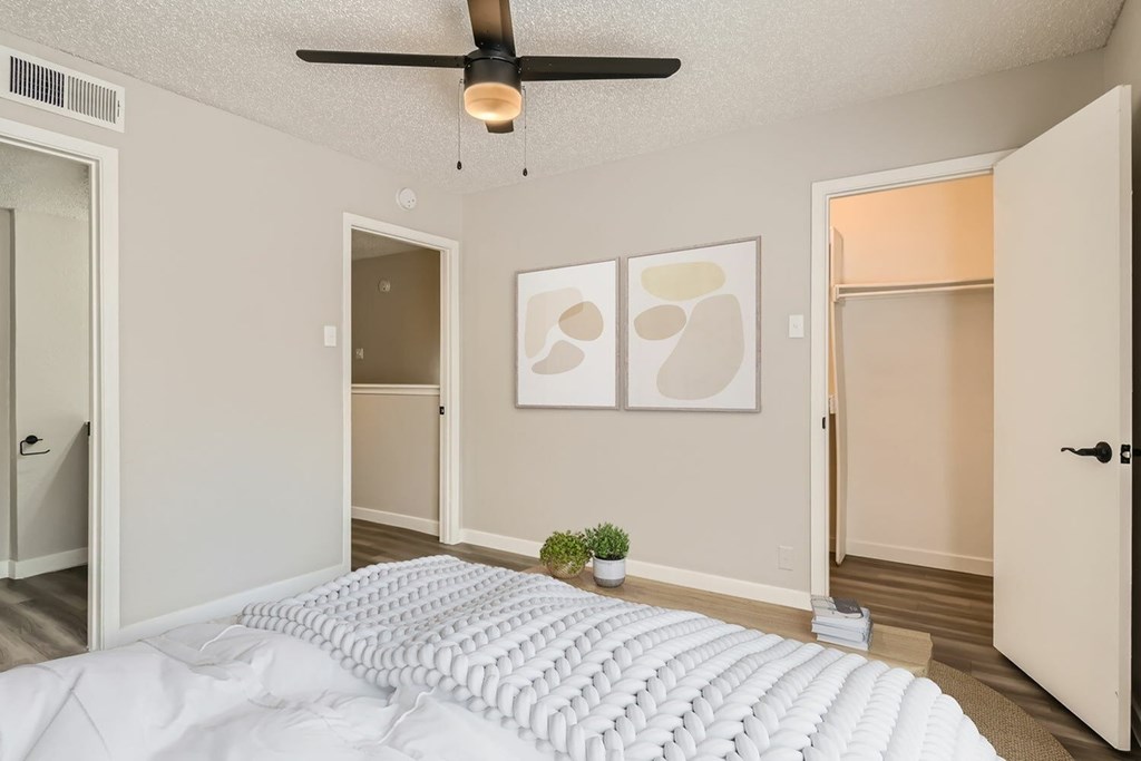 A bedroom with a white bedspread and a ceiling fan.