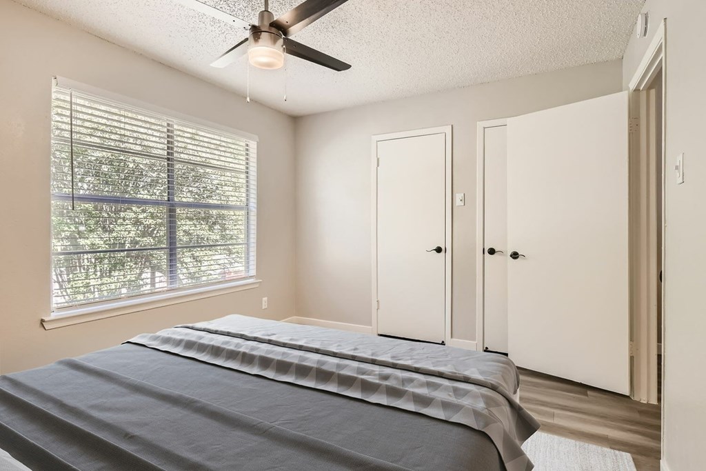 A bedroom with a bed, a window with blinds, and a ceiling fan.
