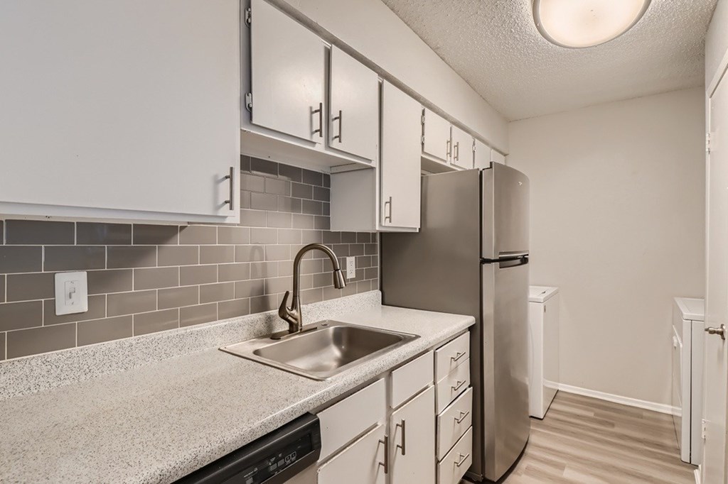 A kitchen with a sink, refrigerator, and cabinets.