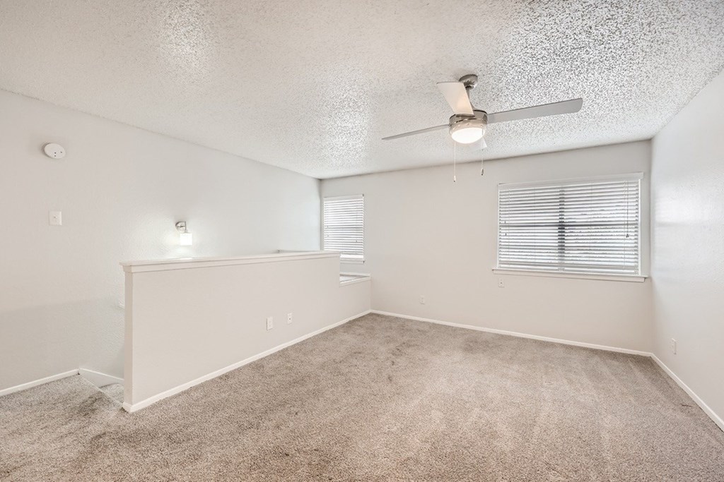 A room with a carpeted floor and a ceiling fan.