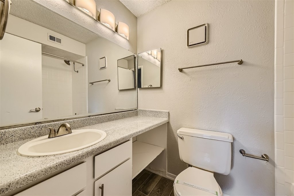 A white bathroom with a toilet, sink, mirror and towel bar.