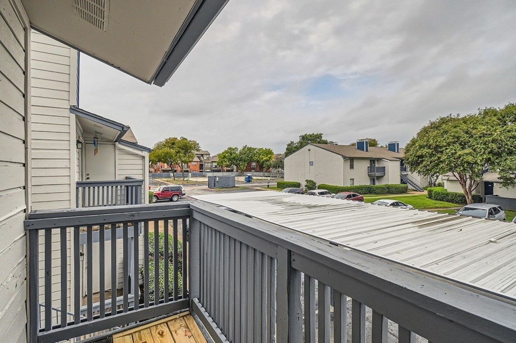 A balcony with a metal railing overlooks a parking lot and houses.