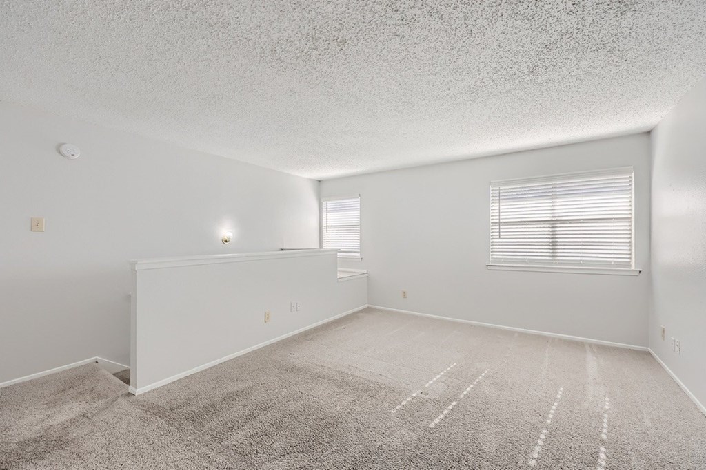 A sparsely furnished room with a carpeted floor and two windows.