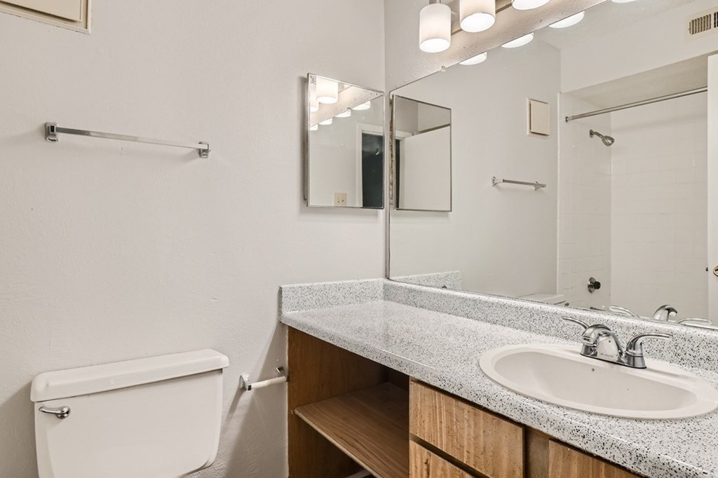 A white bathroom with a sink, mirror, and toilet.