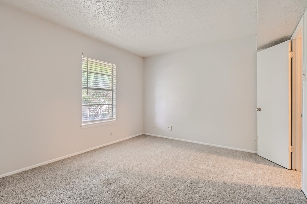 A room with a carpeted floor, a window with blinds, and a closed door.