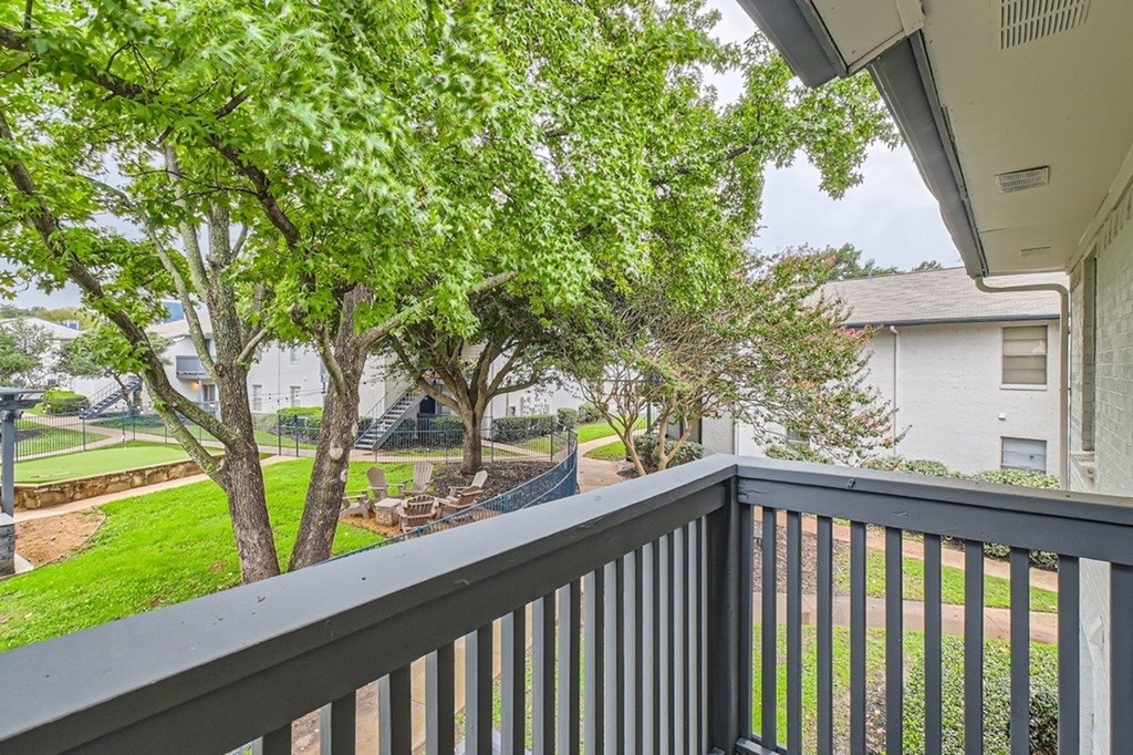 A balcony with a black railing overlooks a tree and a yard.