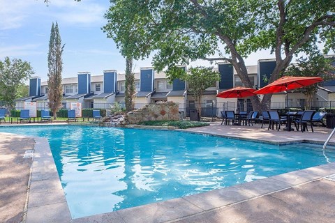 A swimming pool surrounded by trees and chairs with umbrellas.