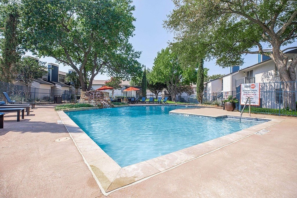 A small pool surrounded by trees and a fence.