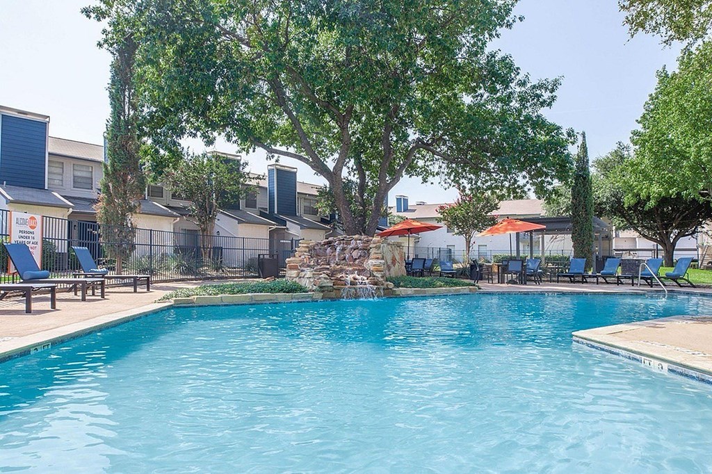 A swimming pool surrounded by trees and chairs.