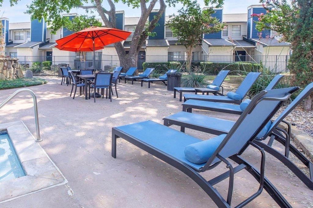 A poolside area with blue lounge chairs and an umbrella.