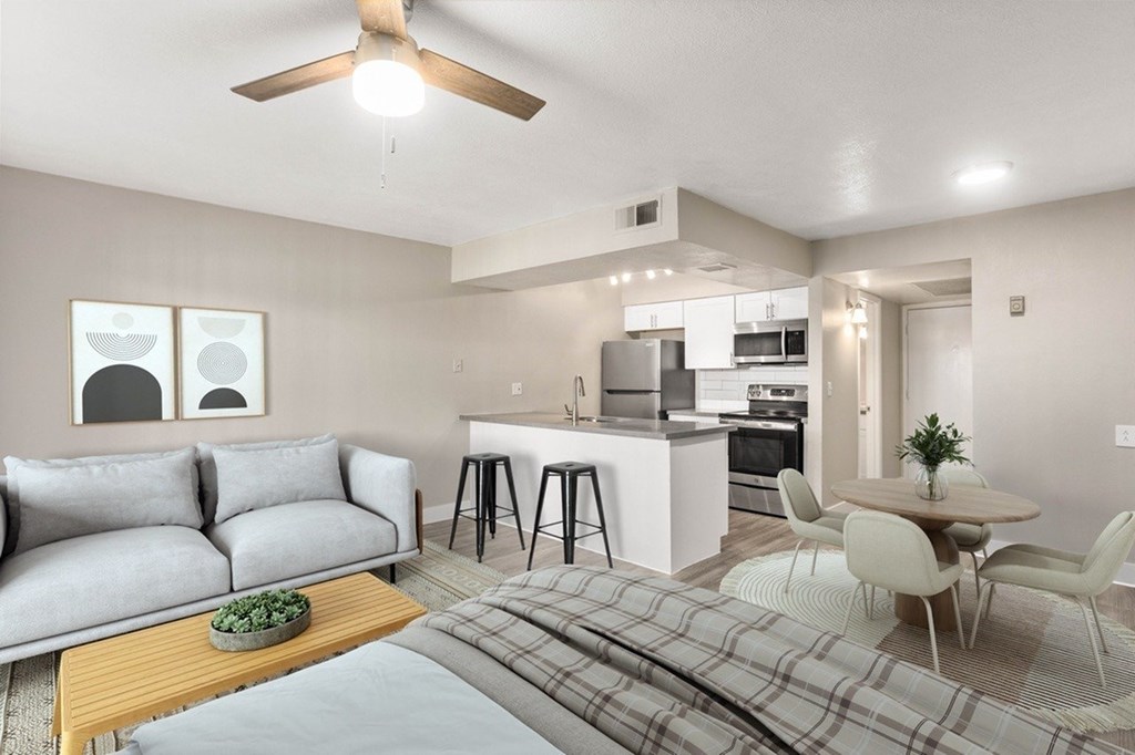 A modern living room with a grey sofa, a wooden coffee table, and a kitchen area in the background.