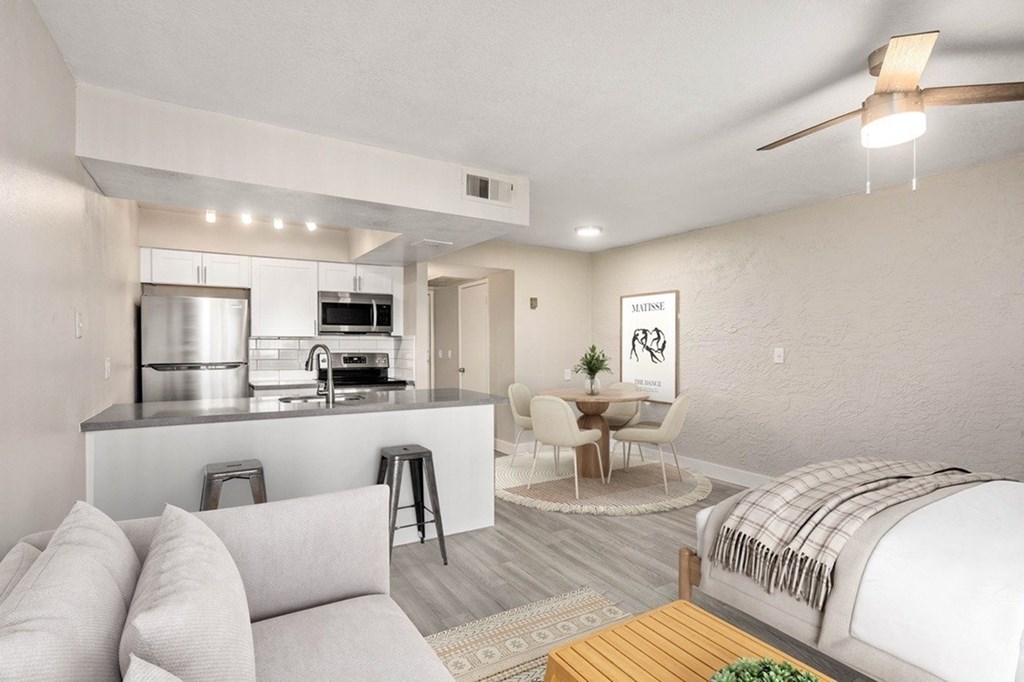 A well-lit, modern kitchen and living room with a bed in the corner.