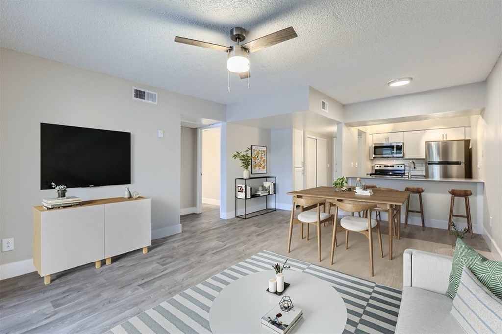 A living room with a television, a dining table, and a kitchen area in the background.