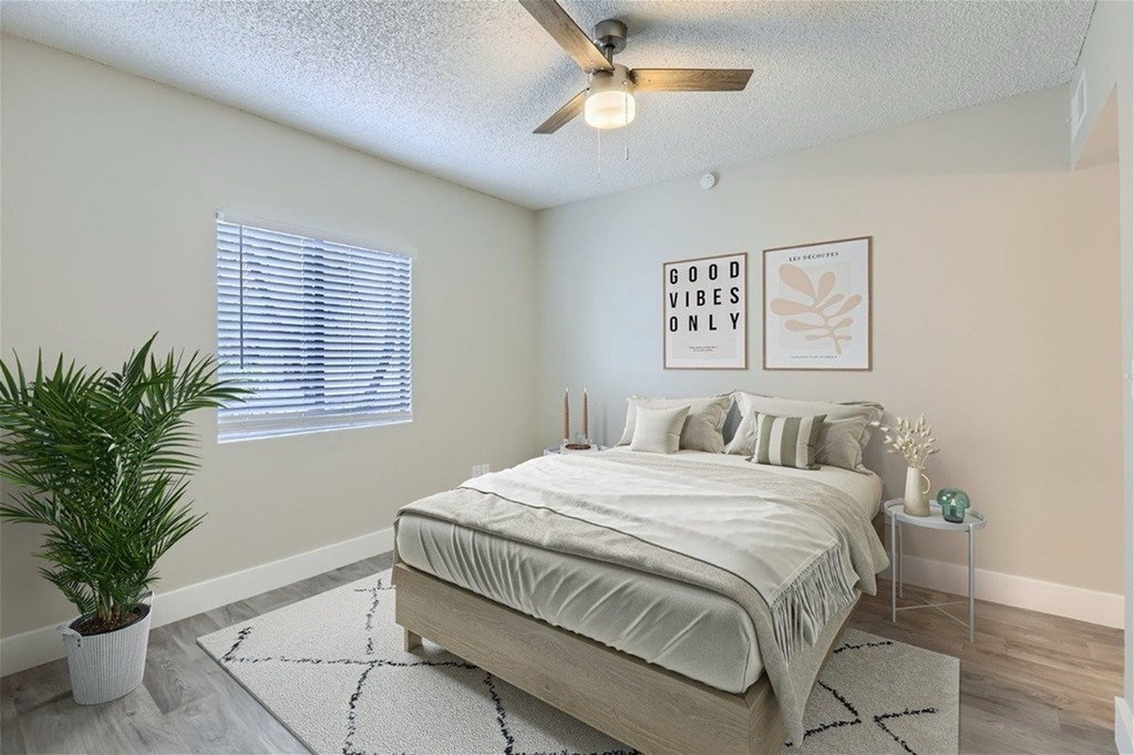 A bedroom with a bed, a plant, and two framed pictures on the wall.