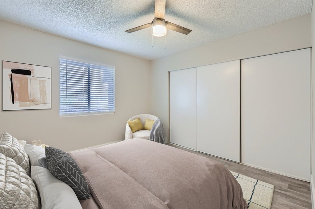 A bedroom with a bed, a chair, and a ceiling fan.