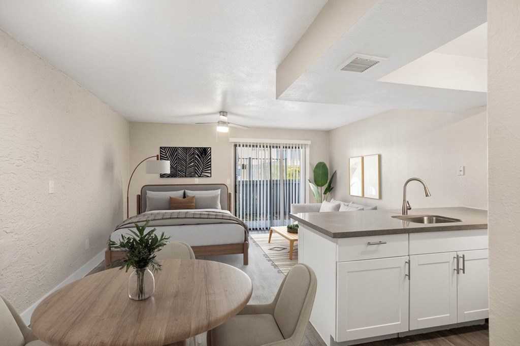 A modern kitchen with a dining table and chairs in the foreground and a bedroom in the background.