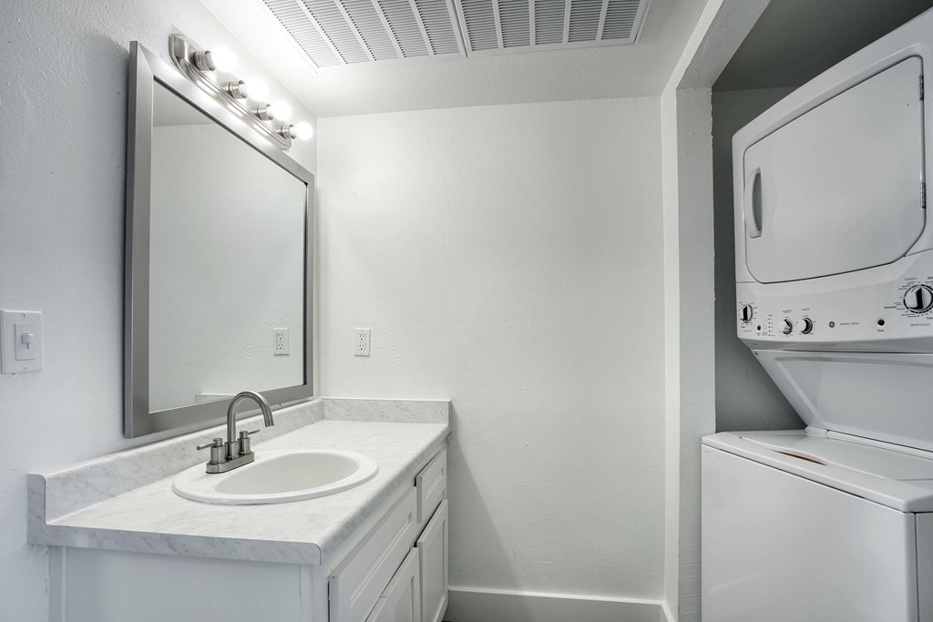 A white bathroom with a sink, mirror, and a washer and dryer.