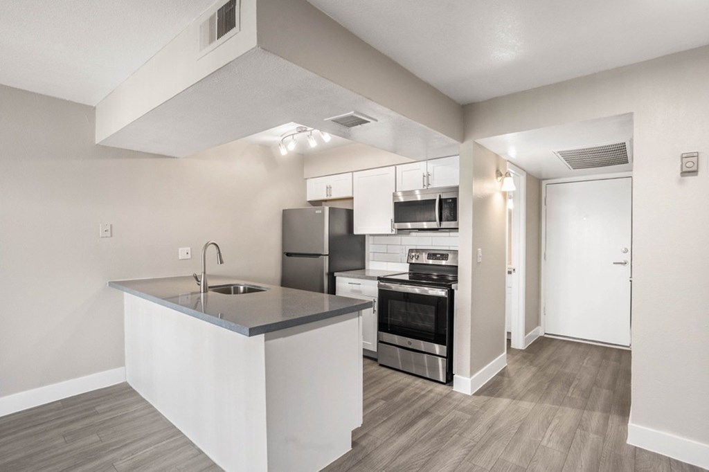 A modern kitchen with stainless steel appliances and a wooden floor.