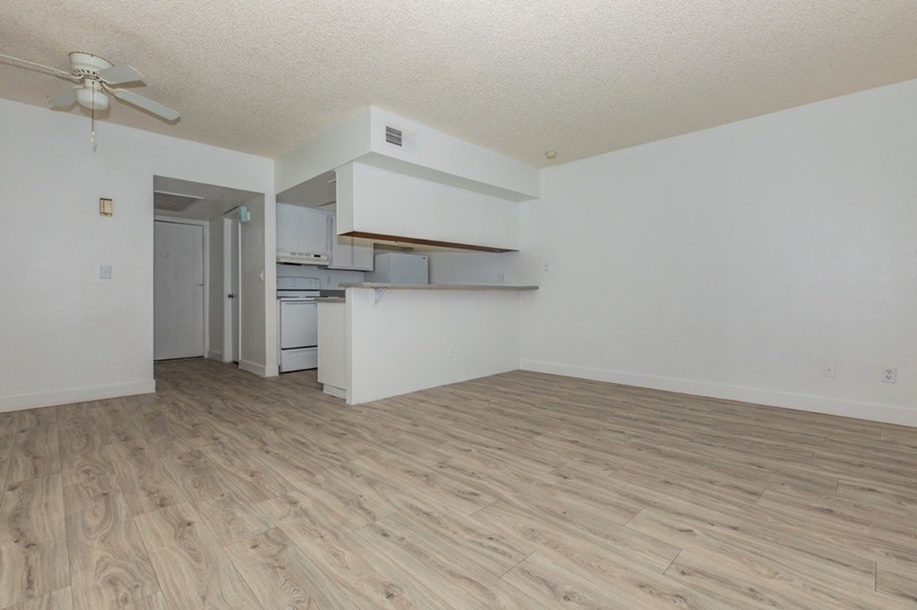 A room with a ceiling fan and a kitchen area with white cabinets.