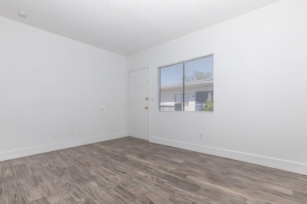 A room with a wooden floor and a window showing a building outside.
