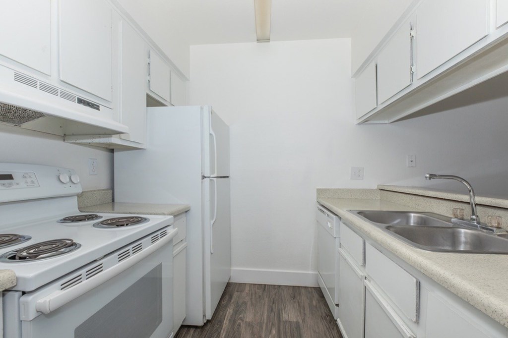 A white kitchen with a stove, refrigerator, and sink.