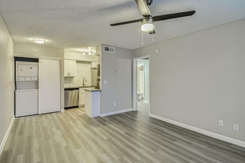 A kitchen with white cabinets and a white fridge is visible from a living room.