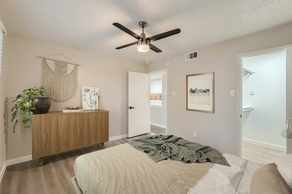 A bedroom with a bed, a ceiling fan, and a plant on a wooden dresser.