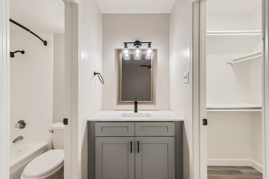 A bathroom with a white toilet, a sink with a mirror above it, and a grey cabinet.