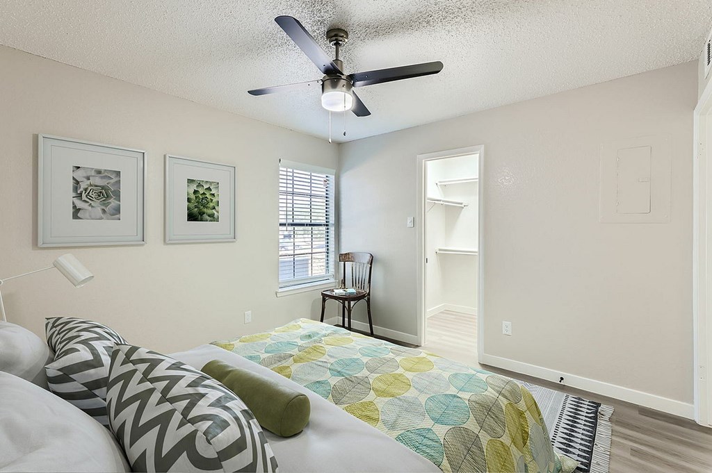 A bedroom with a bed, pillows, a ceiling fan, and two pictures on the wall.