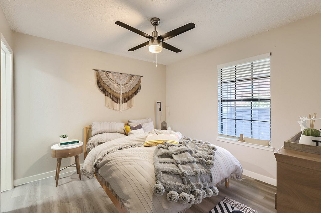 A bedroom with a bed, a ceiling fan, and a window with blinds.