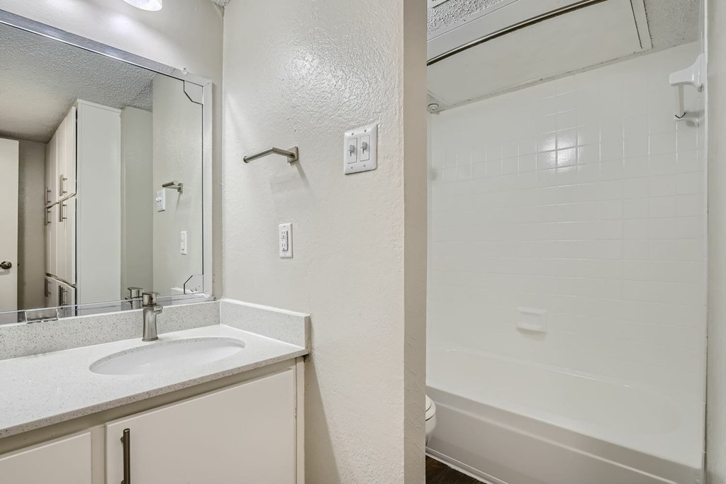 A white bathroom with a sink, mirror, and shower.