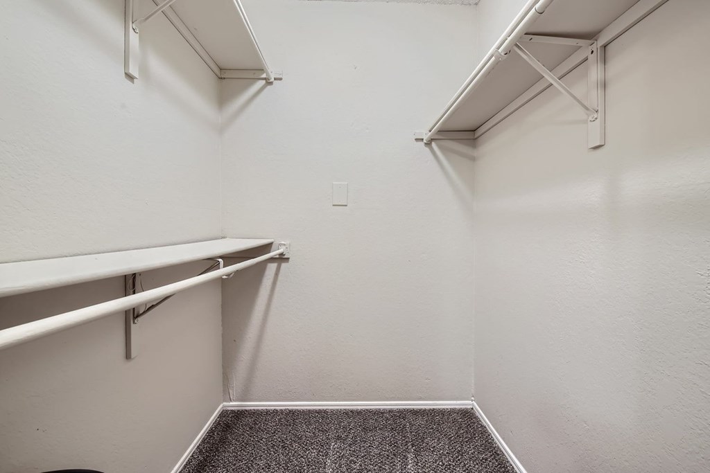 A white wall with a grey carpeted floor and a white shelving unit.