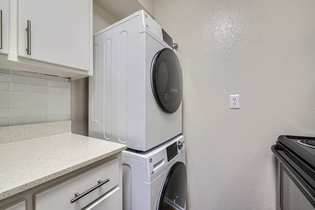 A white washing machine is stacked on top of a white dryer in a kitchen.