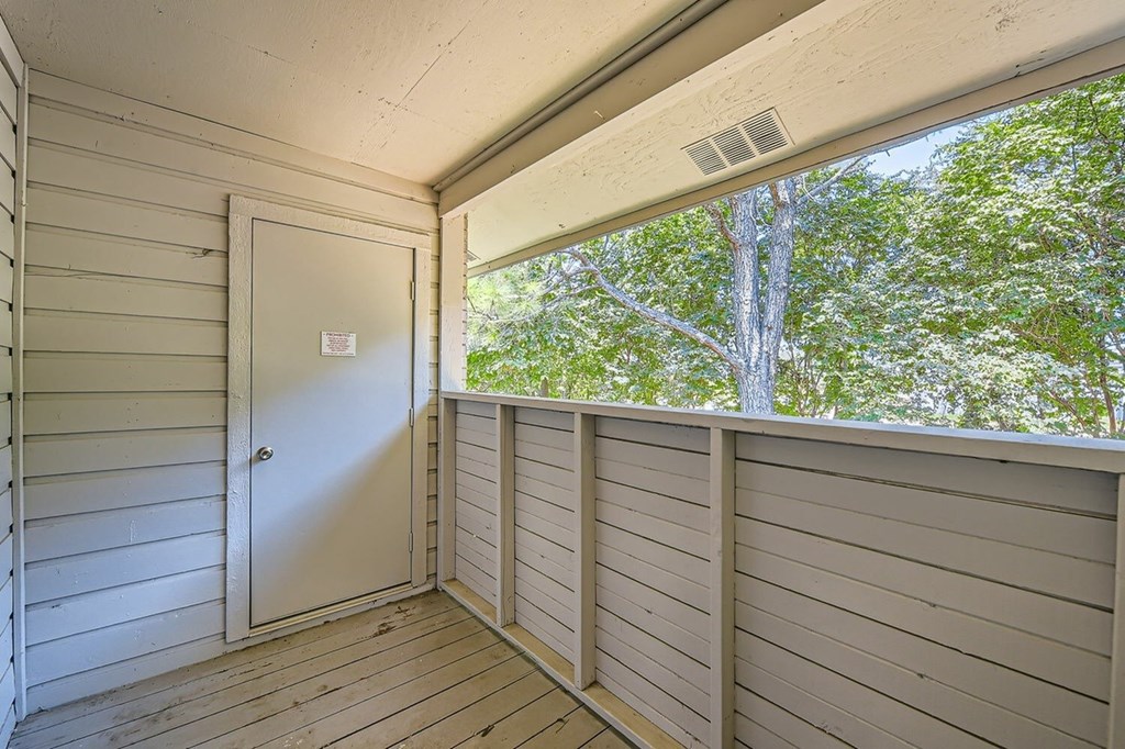 A white door is on the left of a balcony with a view of trees.