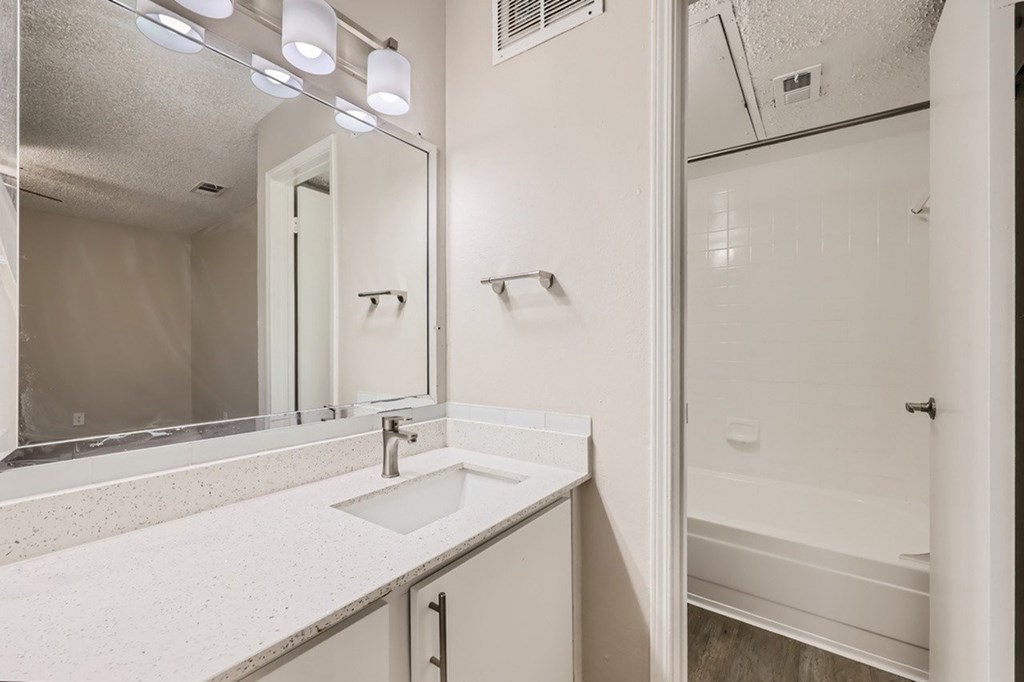 A white bathroom with a sink, mirror, and shower.