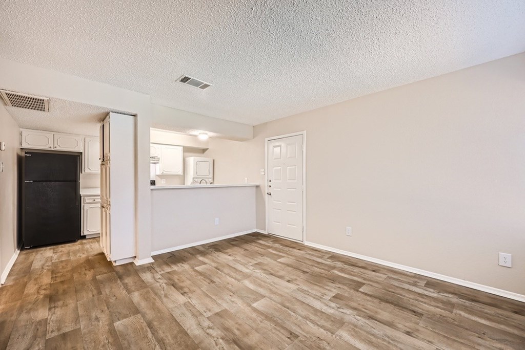 A room with a black fridge and wooden flooring.