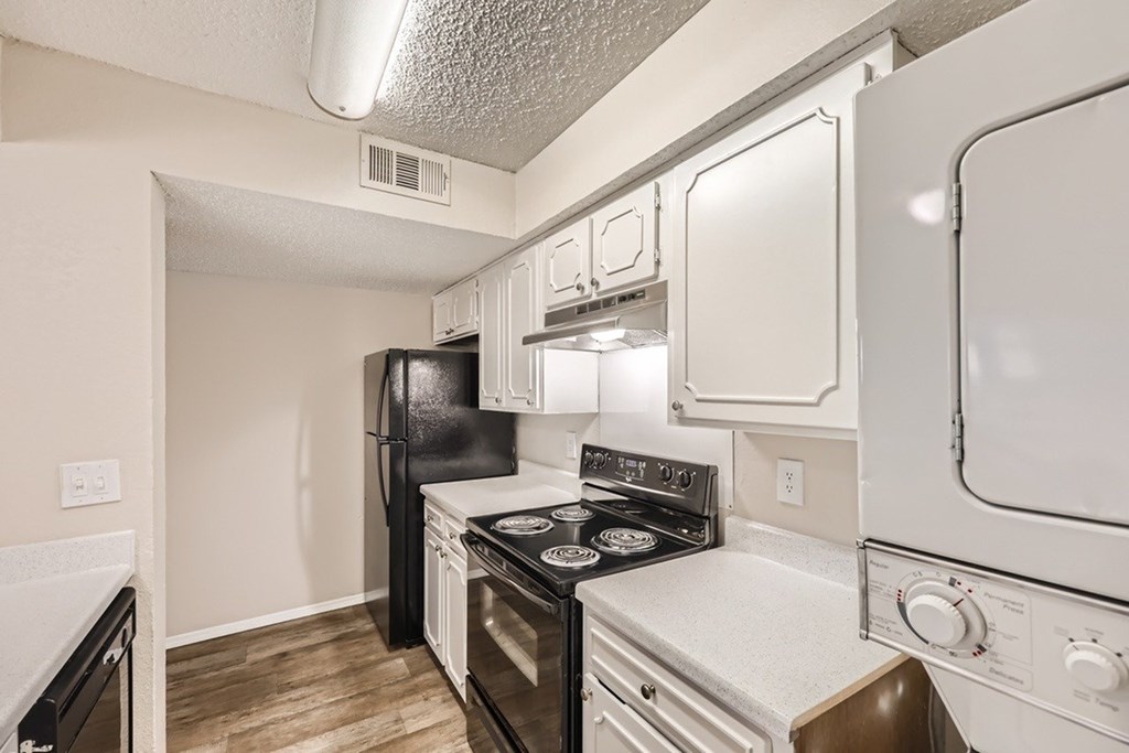 A kitchen with a black refrigerator, white stove, and white oven.
