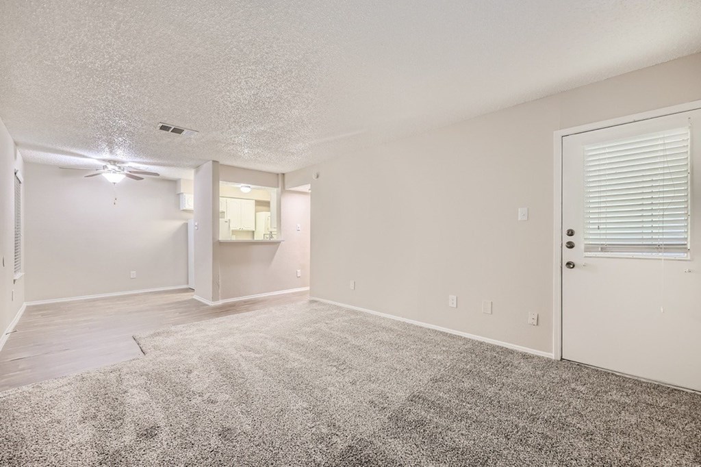 A sparsely furnished room with a carpeted floor and a ceiling fan.