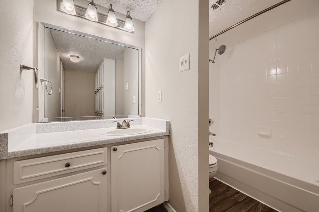 A white bathroom with a sink, mirror, and bathtub.