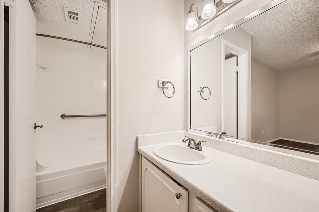 A white bathroom with a sink, mirror, and bathtub.