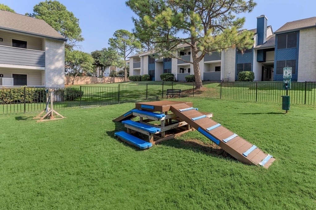 A playground with a slide in the middle of a grassy area.
