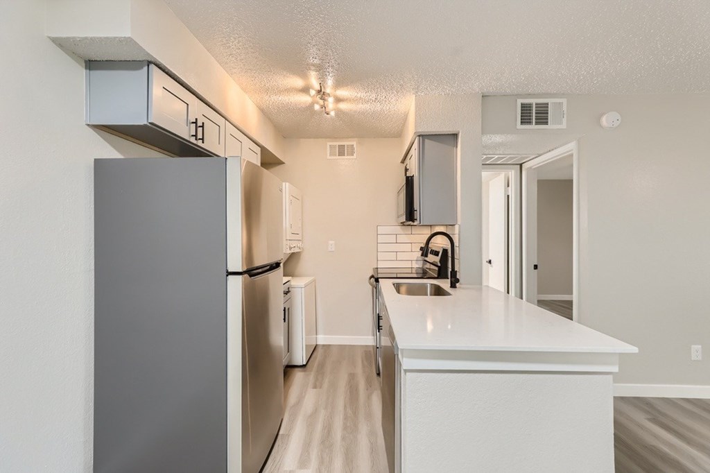 A kitchen with a refrigerator, sink, and cabinets.