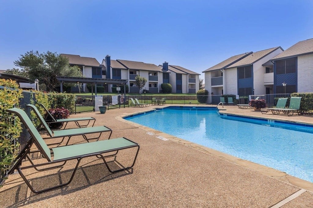 A pool area with lounge chairs and a building in the background.