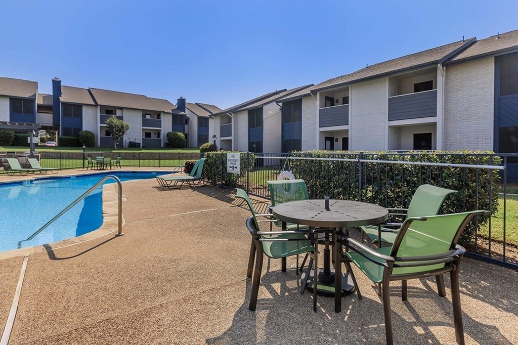 A poolside table with chairs is in front of apartment buildings.